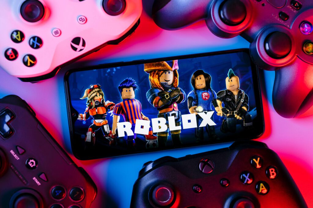 2GRTTTT Roblox is an online game platform and game creation system. A smartphone with the Roblox logo on the screen surrounded by gamepads.